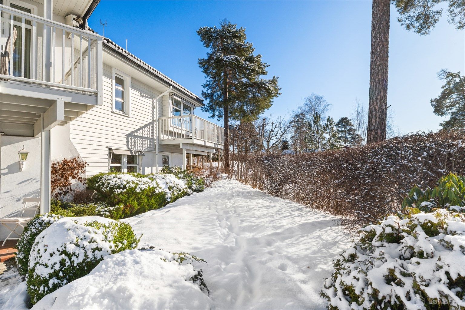 Det er fint plenareal på vestsiden av boligen, omkranset av hekk og med ulike vekster i bed