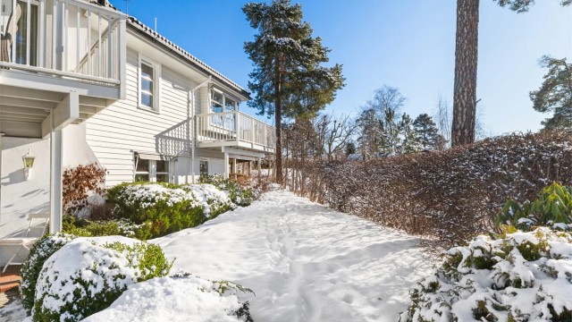 Det er fint plenareal på vestsiden av boligen, omkranset av hekk og med ulike vekster i bed