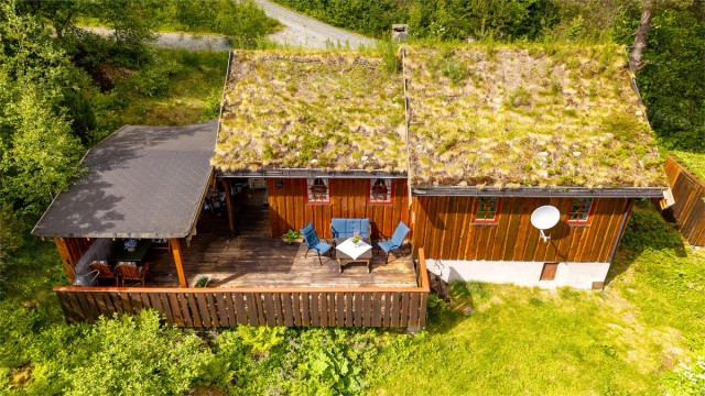 Hytta har yttertak tekket med torv og utvendig stående villmarkspanel.