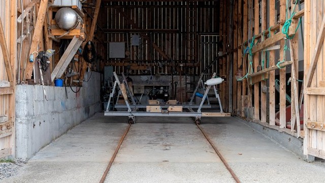 Adkomst gjennom to sidehengslede treporter, hver med en bredde på ca. 4,2 meter, som åpner opp hele fronten av naustet.