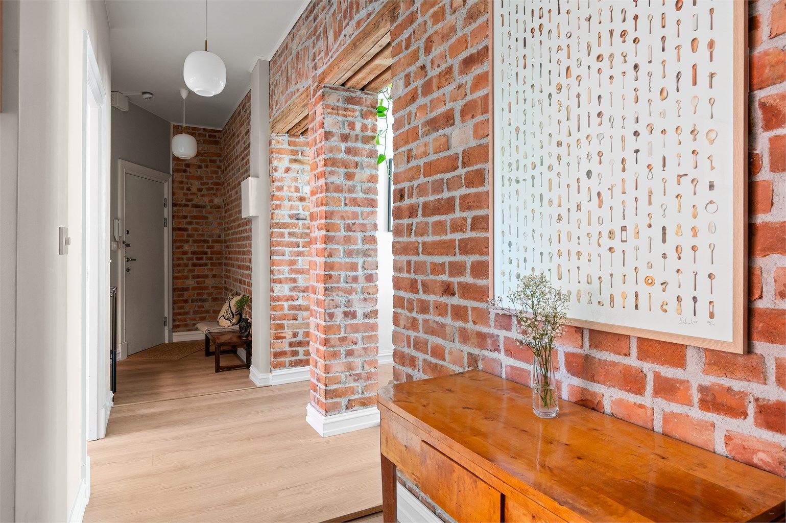 Den åpne gangen har eksponert teglstein som viderefører leilighetens karakter.