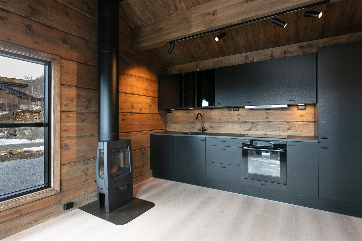 Moderne kjøkken fra JKE Design med sorte, glatte fronter og integrerte hvitevarer. Peisovnen fra Dovre gir en lun atmosfære.