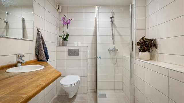Gulv med fliser, elektrisk gulvvarme. Innredet med vegghengt klosett, servant nedfelt i heltre benkeplate og dusjhjørne med svingbare glassdører. Opplegg for vaskemaskin