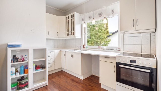 Lys kjøkkeninnredning med glatte fronter og benkeplate med laminert overflate. Nisje for komfyr og plass til frittstående kjøleskap.