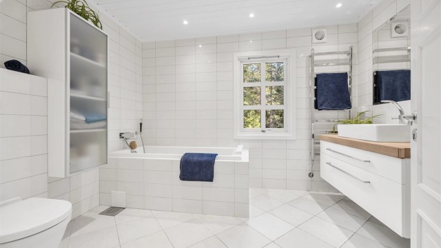 Lekkert flislagt bad med badekar og dusjhjørne.