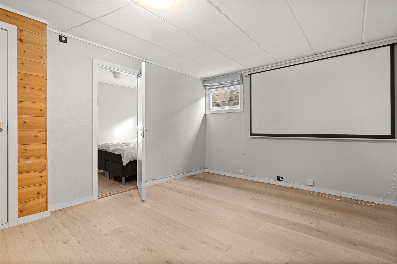 Innredet kjellerrom med projektorlerret og laminat på gulv.