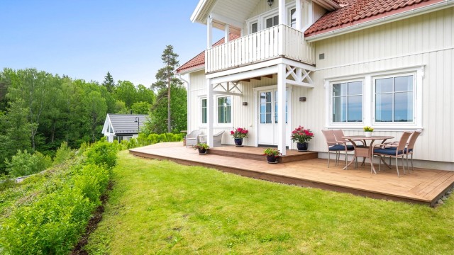 Koselig hage med plen, terrasse, hekk og beplantninger.