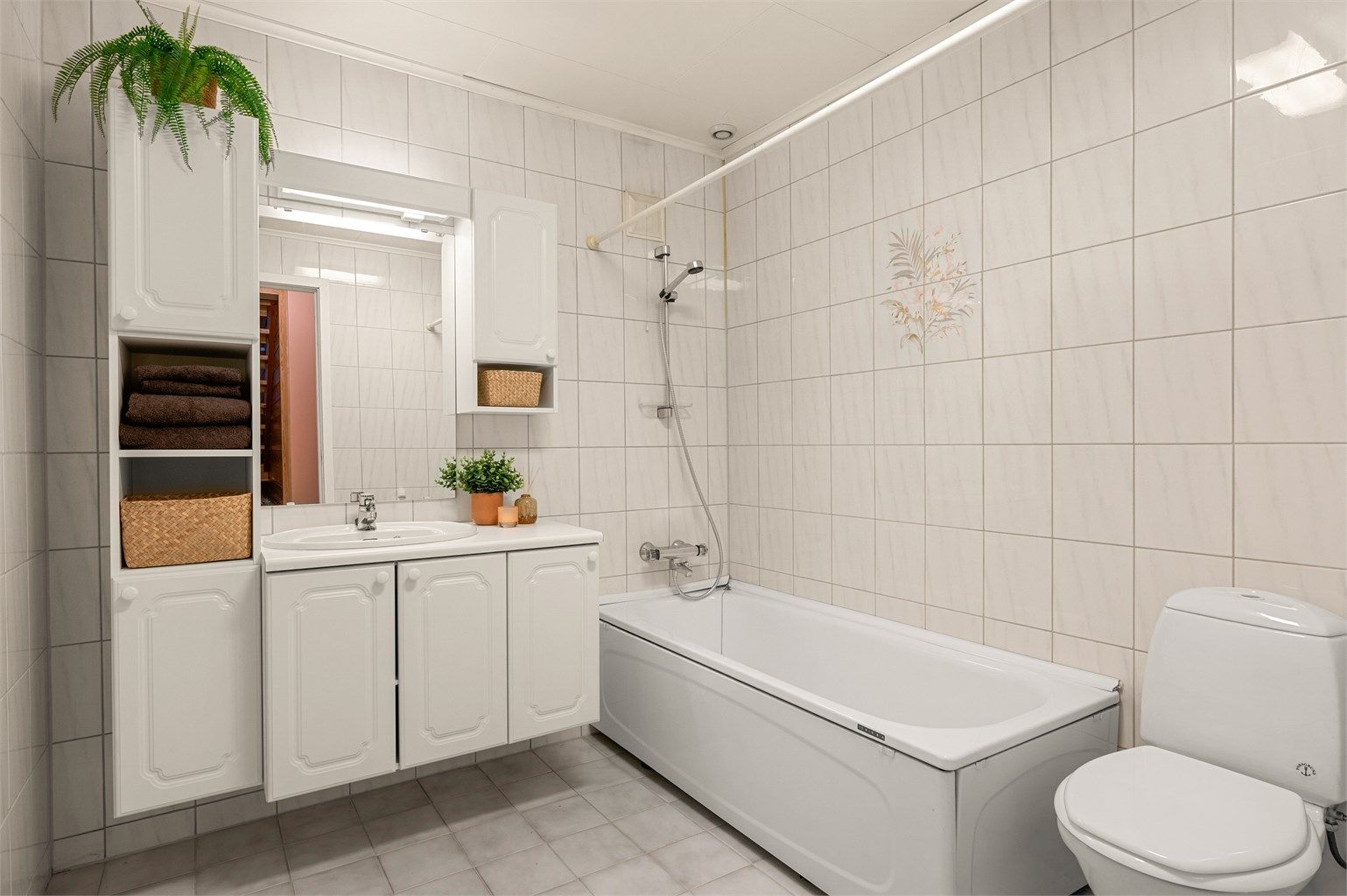 Badet i kjelleren har flislagte overflater, gulvvarme, badekar, servantinnredning og toalett.