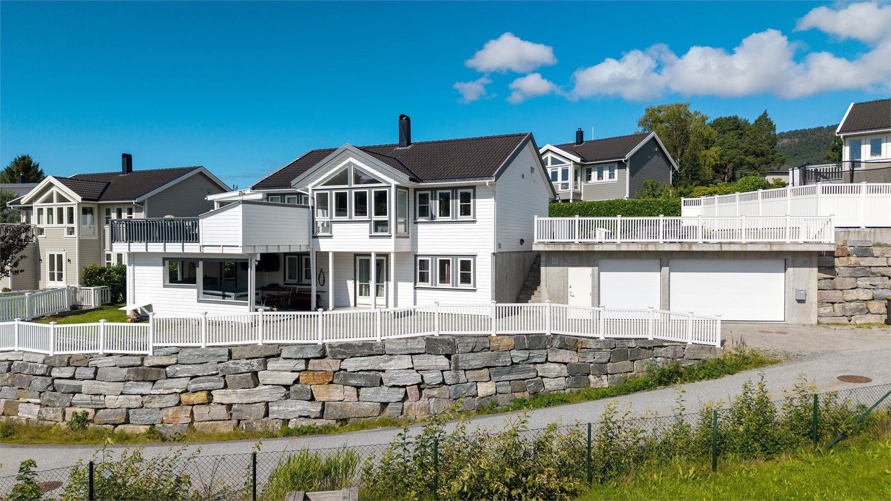 Eiendommen er rammet inn av en forseggjort forstøtningsmur i naturstein og hvitt gjerde.