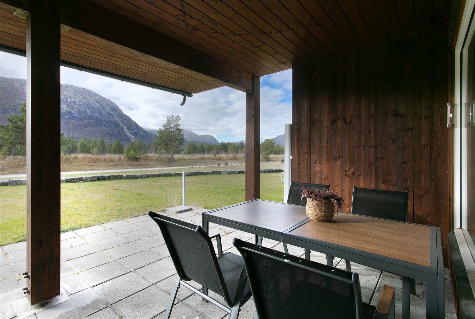 Overbygd markterrasse i betongheller med åpent utsyn mot fjellene.