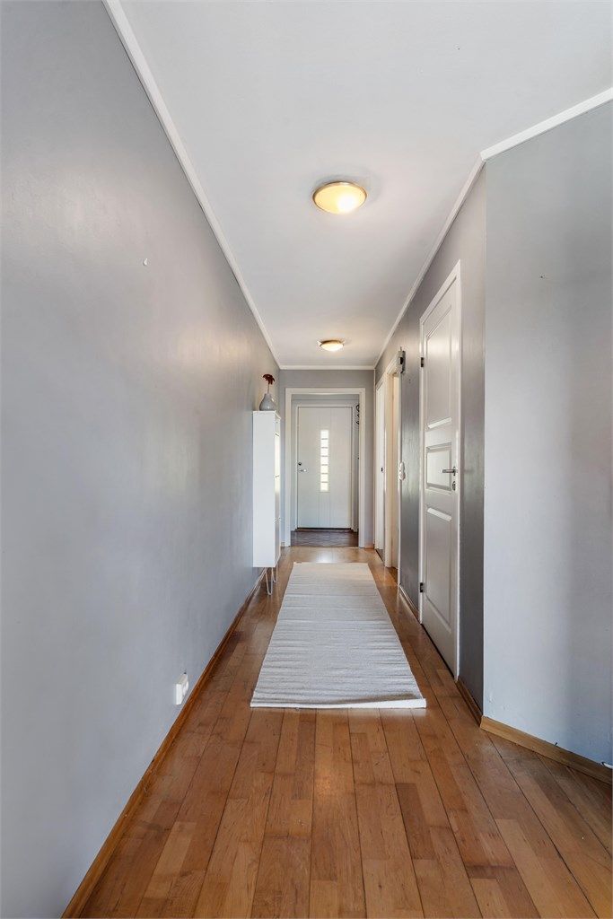 Gangen binder sammen soverom, bad og oppholdsrom, med parkett på gulvet.