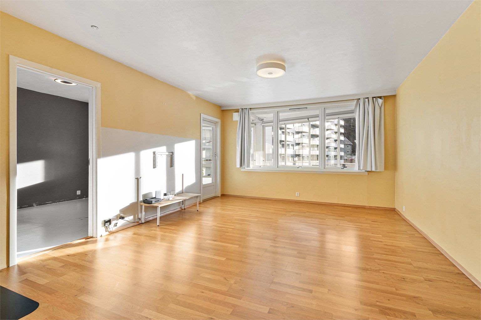 Lys og romslig stue med vindu mot innglasset balkong