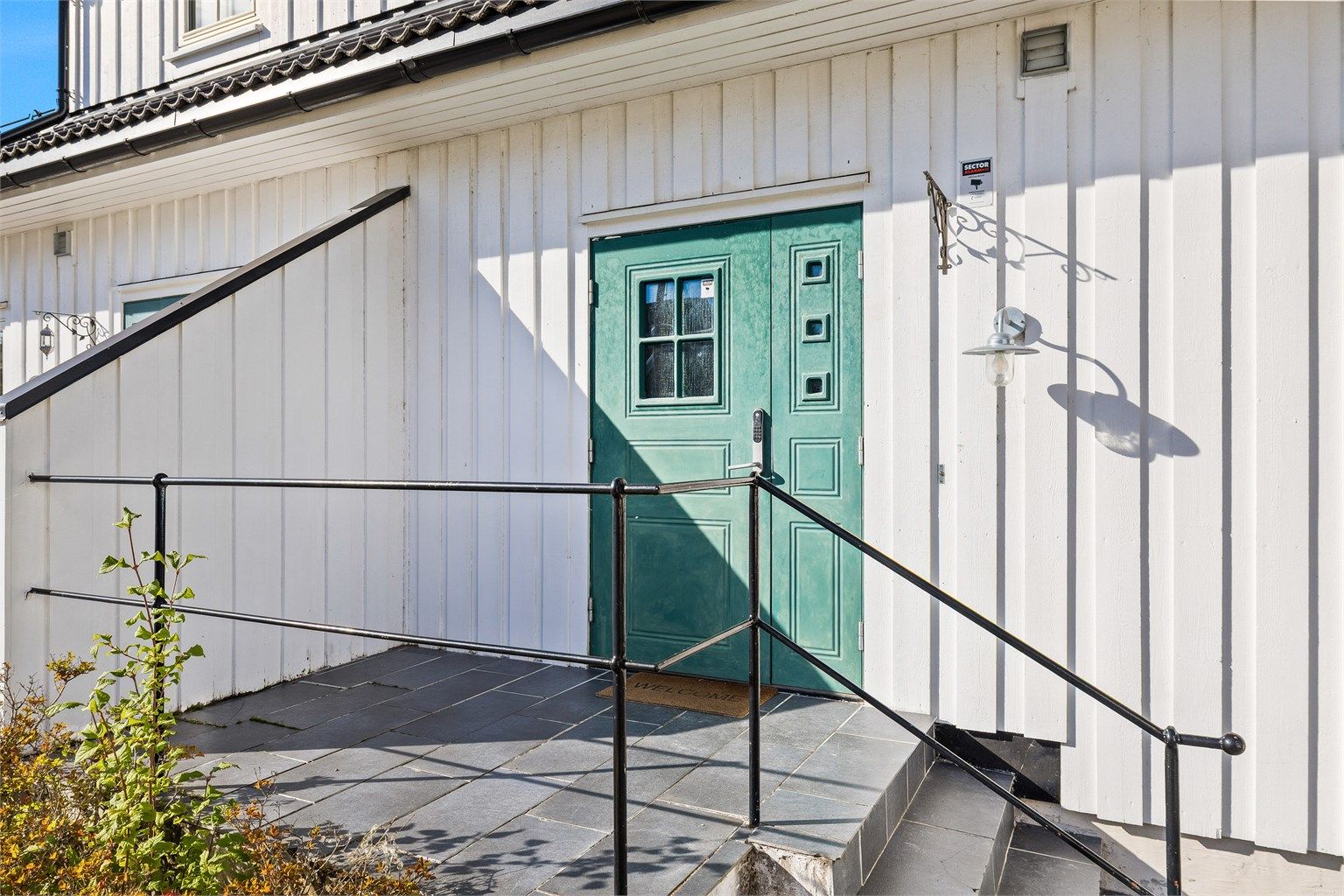 Rekkverket i sort smijernsstil harmonerer godt med dørens uttrykk og bidrar til et helhetlig og klassisk utseende.