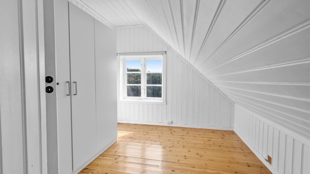 Innredet soverom på loftet med plassbygd oppbevaring og tregulv.