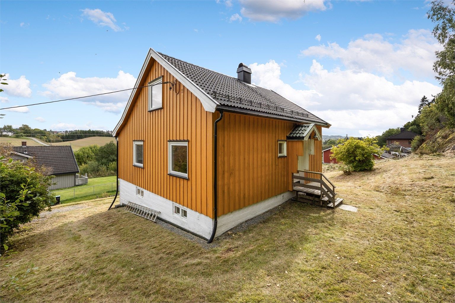 Overbygget inngangsparti med utvendig trapp i tre ved adkomsten i første etasje.