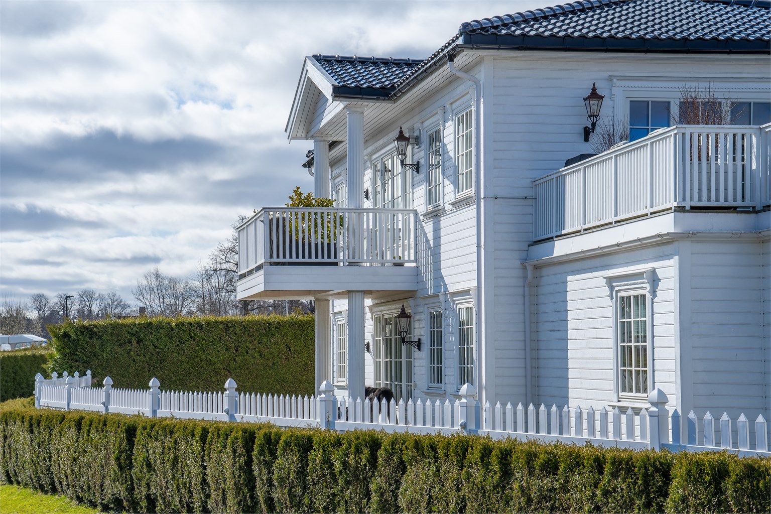 Eiendommen fremstår med et stilrent uttrykk med utebelysning, søyler, glasert takstein og pent opparbeidet hage.