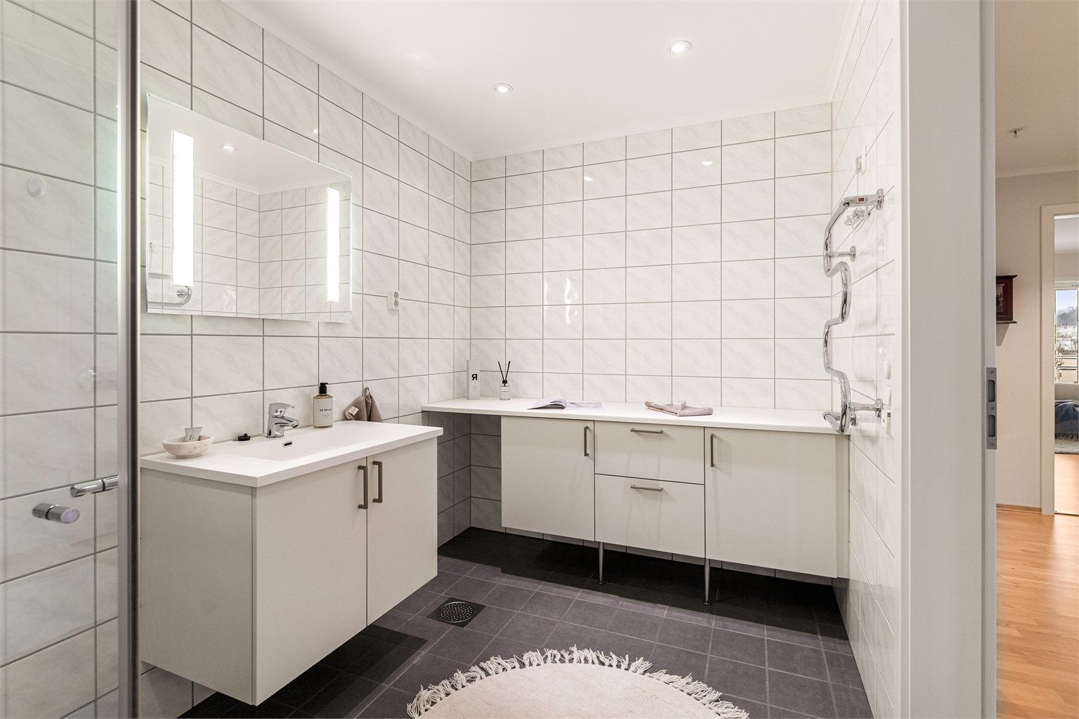 Badet er godt innredet med håndkleholder, servant i innredning, dusjhjørne og toalett. Ekstra skaper med benkeplate for oppbevaring av håndkler etc