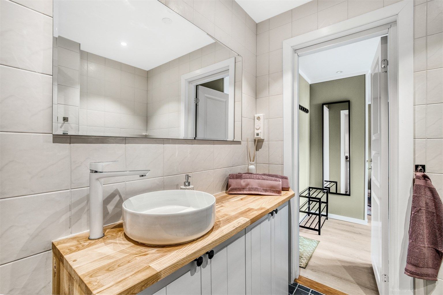 Badet er innredet med en stilren, bollemontert servant på en benkeplate i heltre.