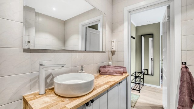 Badet er innredet med en stilren, bollemontert servant på en benkeplate i heltre.