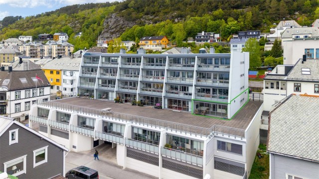 Dronebilde av fasade og leilighetens beliggenhet i 1. etasje på enden mot øst med tilkomst til stor felles terrasse