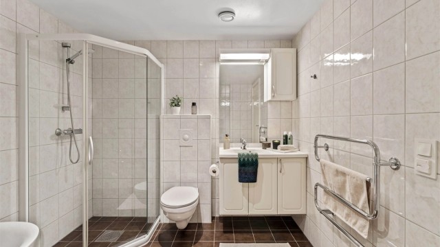 Helfliset bad med gulvvarme, vegghengt toalett og et praktisk dusjhjørne.