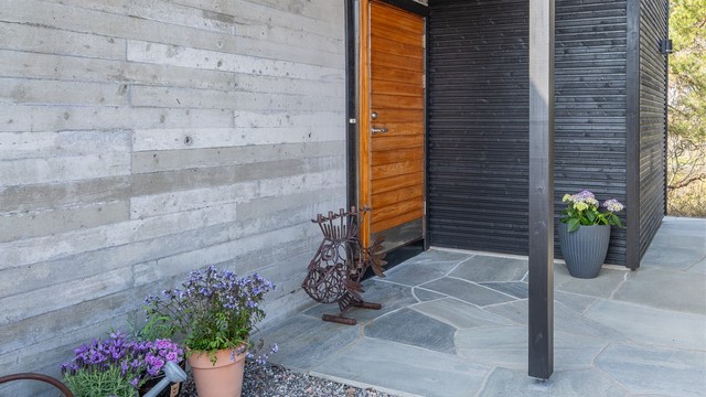 Hovedytterdøren i teak står i stilfull kontrast til den rå betongfasaden og den mørke trekledningen.