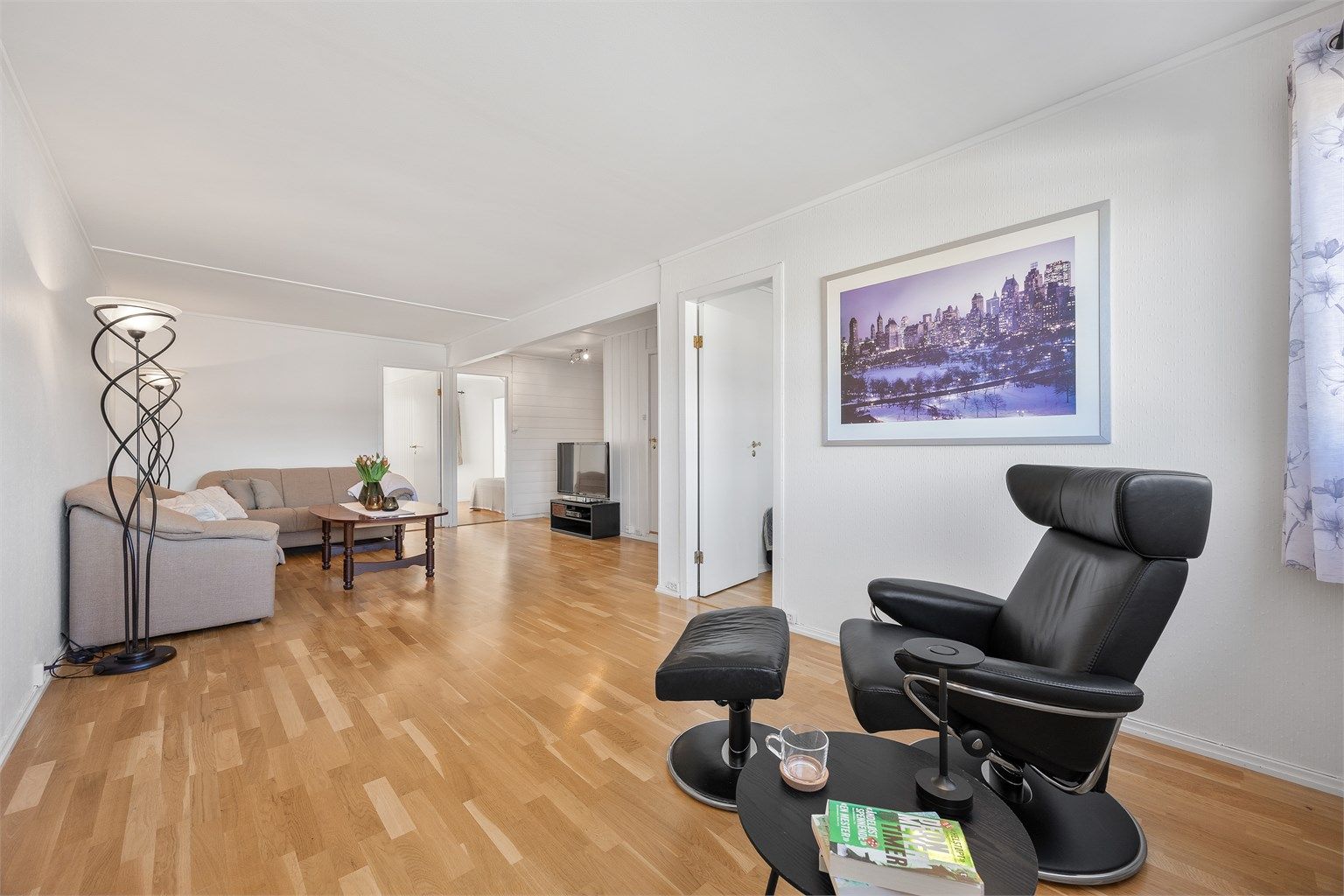 Gjennomgående parkettgulv i stuen og lyse veggflater skaper en helhetlig atmosfære.