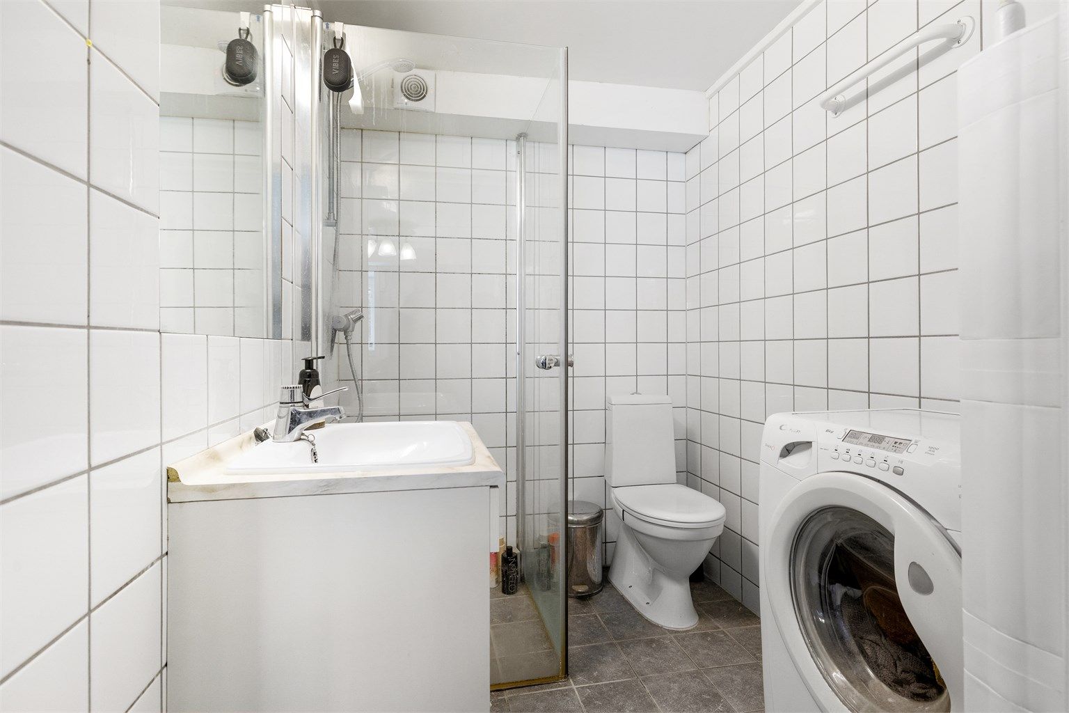 Bad i kjelleren med flislagt gulv med gulvvarme, dusjhjørne og opplegg for vaskemaskin.