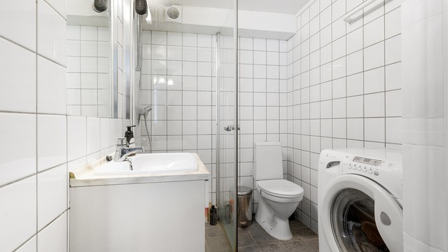 Bad i kjelleren med flislagt gulv med gulvvarme, dusjhjørne og opplegg for vaskemaskin.