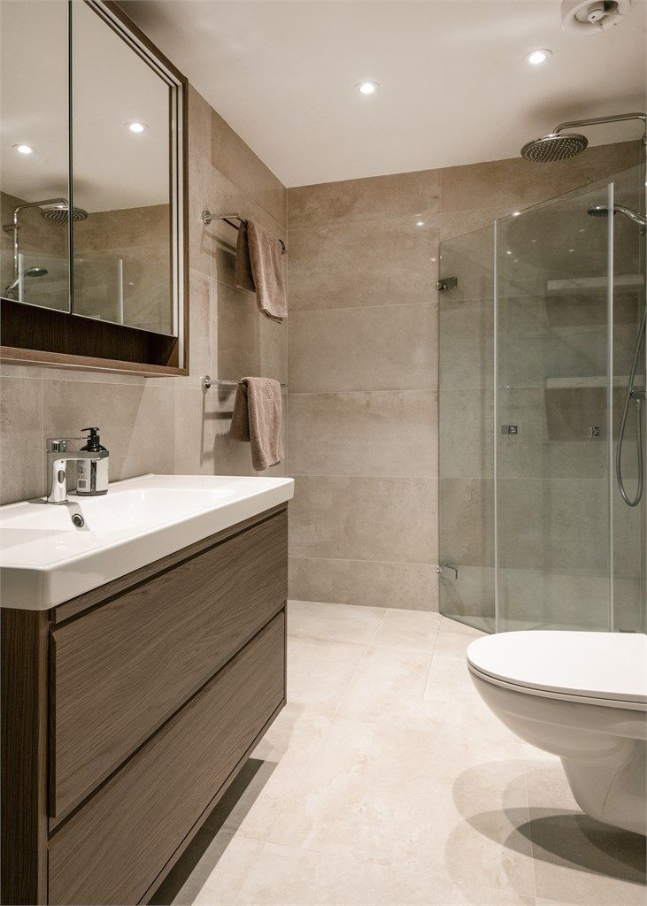 Badet er utstyrt med vegghengt toalett, servantinnredning og et dusjhjørne med innfellbare glassdører.