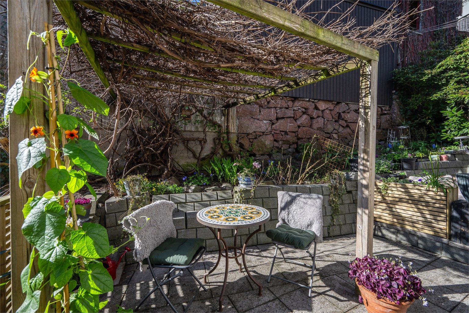 Terrassen er delvis overbygget av en pergola, som gir en hyggelig ramme for uteplassen.