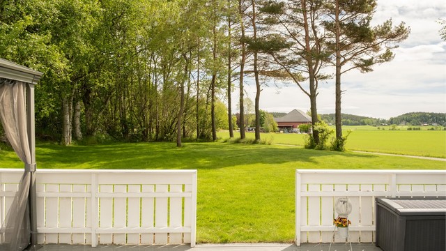 Flott utsyn over egen hage til åkerlandskap og skogkledde åser.