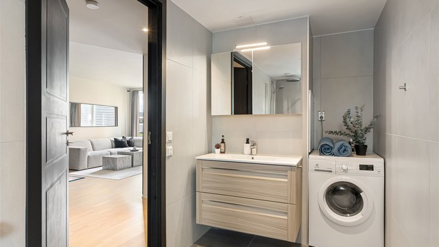 Videre er badet innredet med servantskap med speil og lys, toalett og dusjhjørne med regndusj.