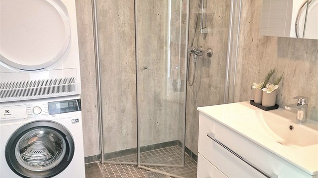 Romslig bad med flislagt gulv med gulvvarme, dusjhjørne og opplegg for vaskemaskin.