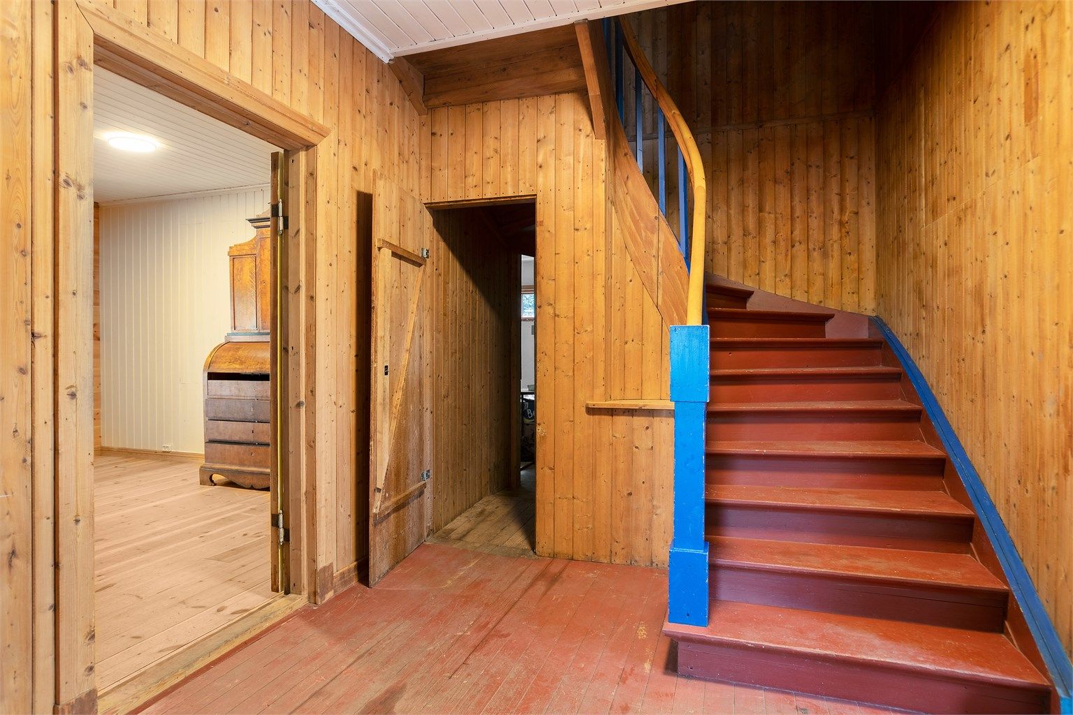 Hall med panelkledde vegger og trapp i trekonstruksjoner.