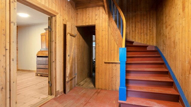 Hall med panelkledde vegger og trapp i trekonstruksjoner.