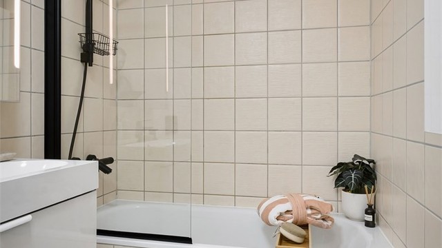 Badet er innredet med vegghengt klosett, servant med innredning, speil med lys og badekar med svingbar glassdør