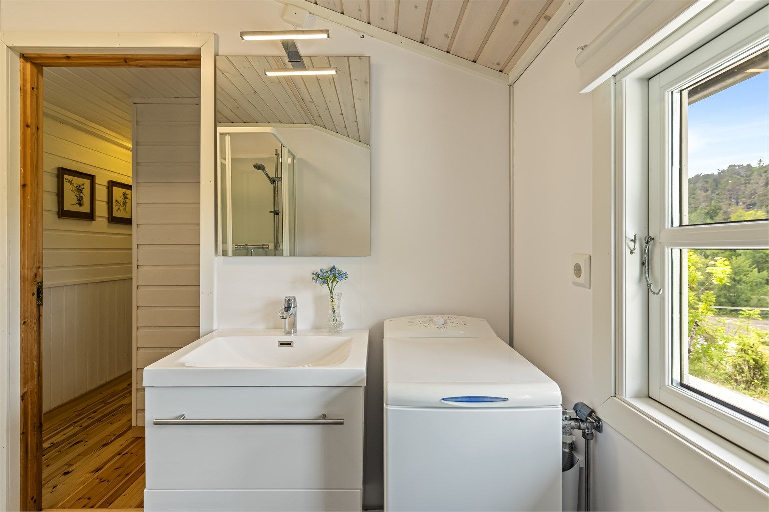 Praktisk innredet bad med heldekkende servant, speil med overlys og opplegg for vaskemaskin.