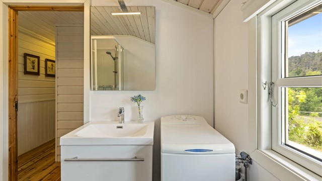 Praktisk innredet bad med heldekkende servant, speil med overlys og opplegg for vaskemaskin.