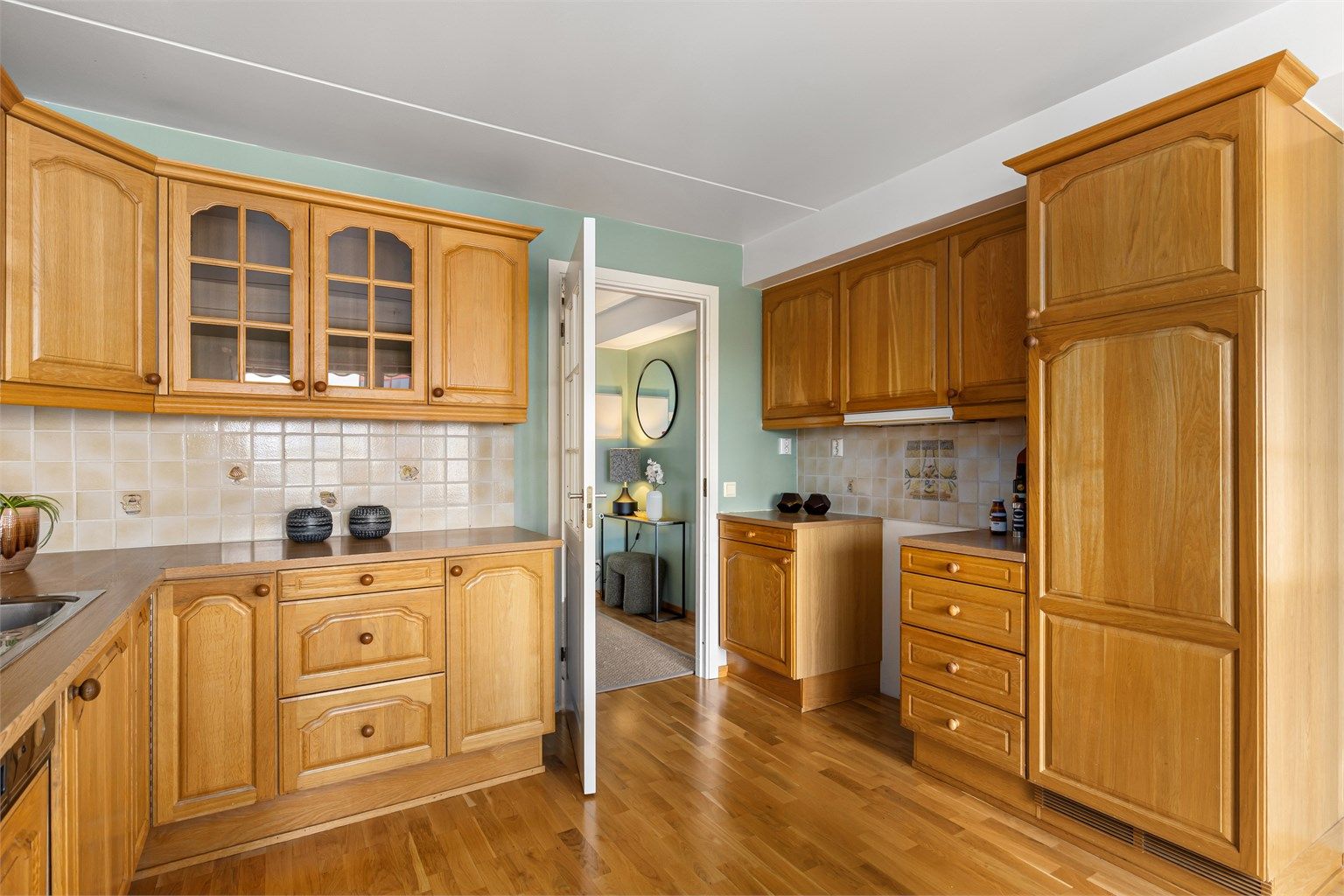 Kjøkkenet har profilerte fronter i heltre eik, med benkeplate i laminat og fliser mellom benk og overskap.