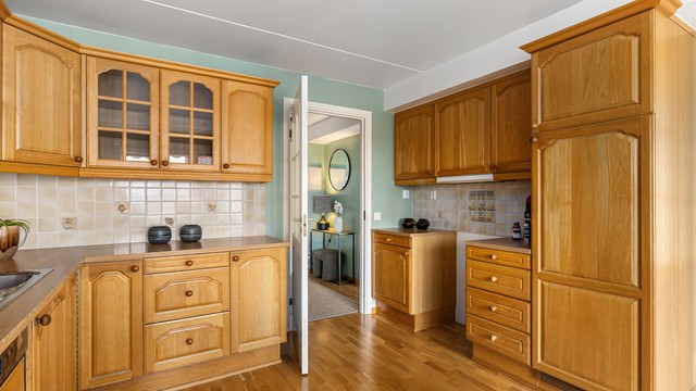 Kjøkkenet har profilerte fronter i heltre eik, med benkeplate i laminat og fliser mellom benk og overskap.