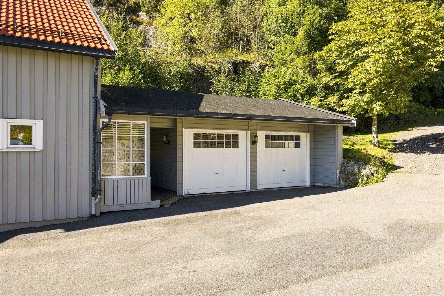 Garasjen har to hvite porter med vindusfelt og saltak tekket med shingel.
