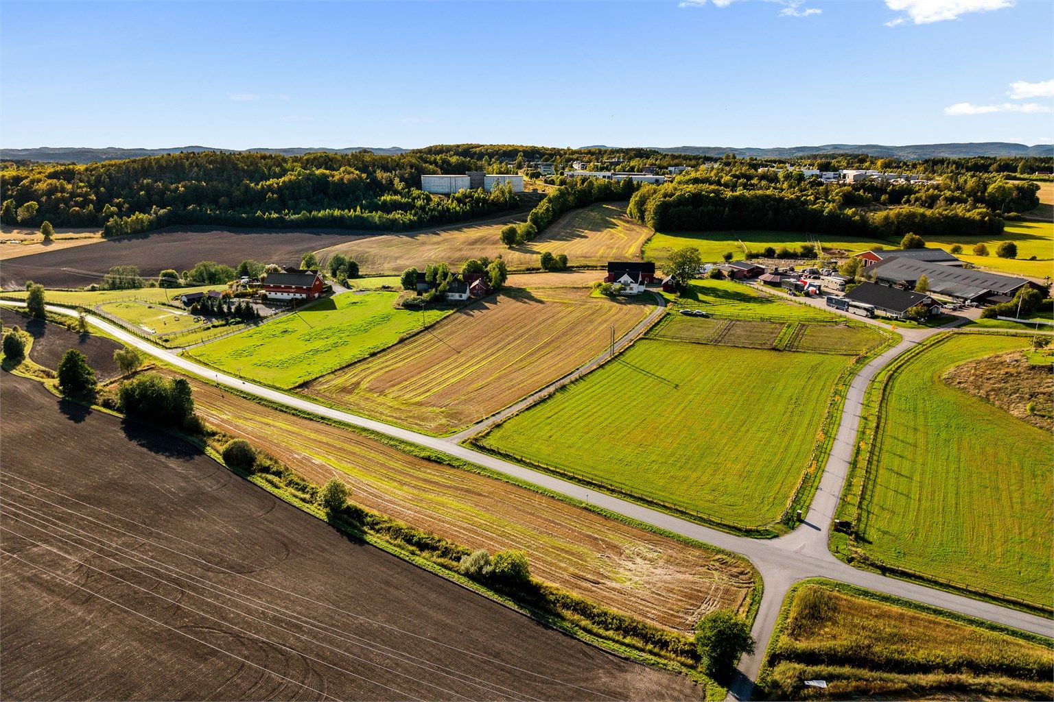 Landbrukseiendom i åpne, landlige omgivelser med våningshus, låve og garasjebygning. Foto: [ Kron Media AS - Karl Filip Kronstad ]