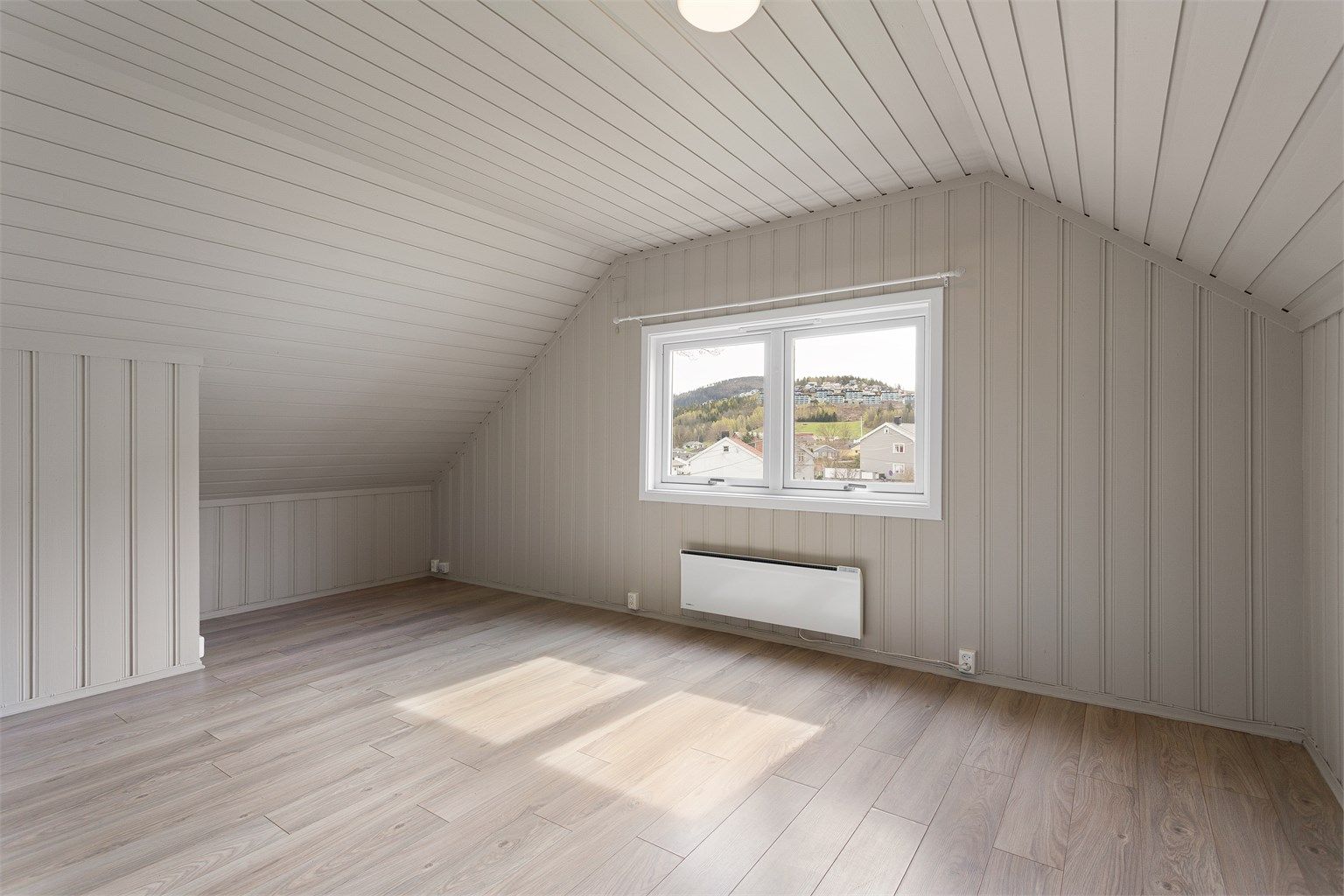 Stuen i loftsleiligheten har malt panel på vegger og i tak, med lagringsplass i kott bak knevegger.