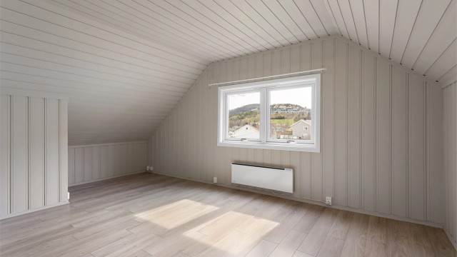 Stuen i loftsleiligheten har malt panel på vegger og i tak, med lagringsplass i kott bak knevegger.