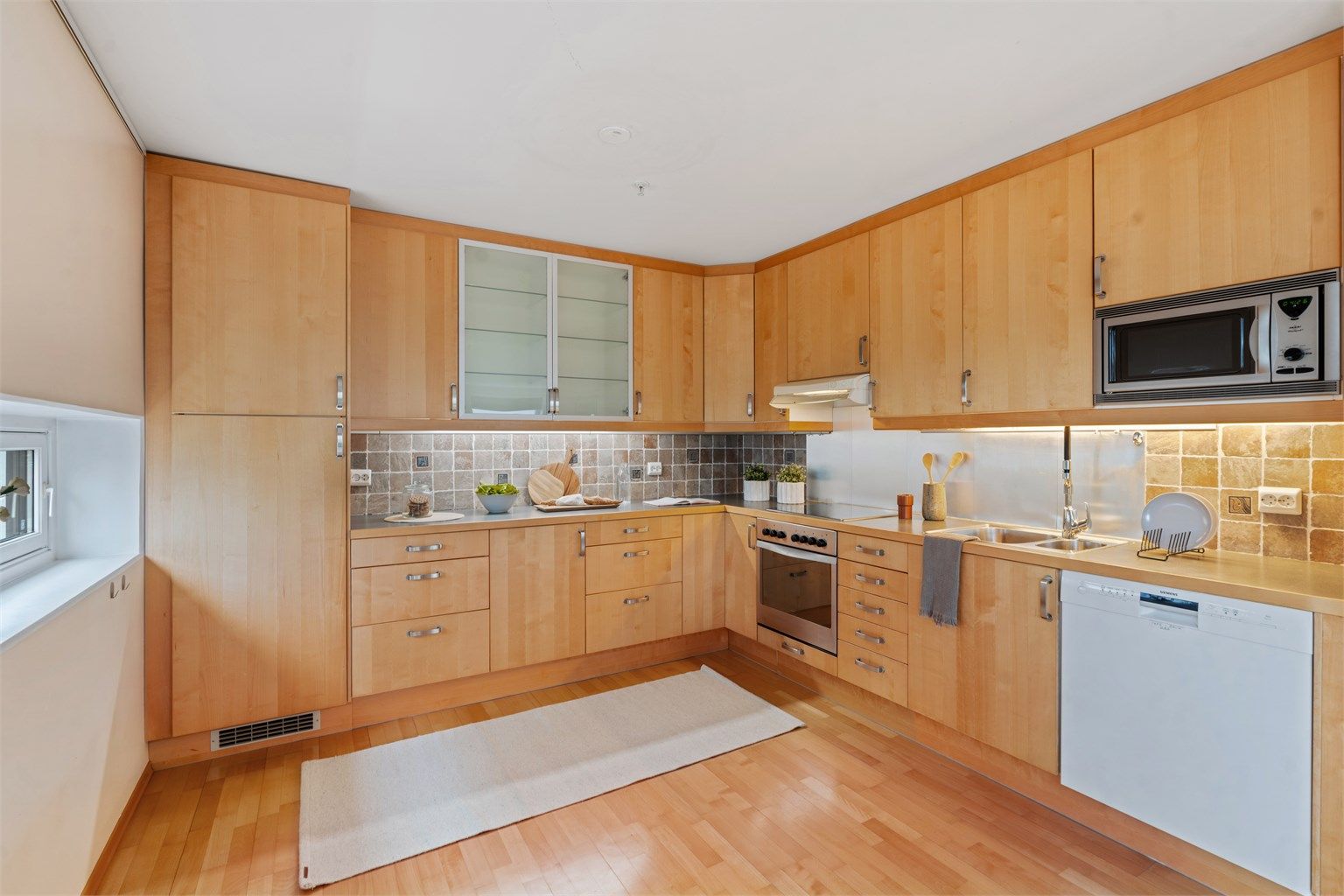 Det er fliser mellom kjøkkenbenk og overskap, samt belysning under overskapene.