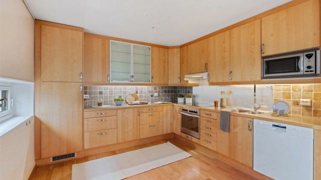 Det er fliser mellom kjøkkenbenk og overskap, samt belysning under overskapene.