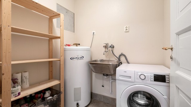 Separat vaskerom med flislagt gulv med gulvvarme, opplegg for vaskemaskin og boligens varmtvannsbereder.