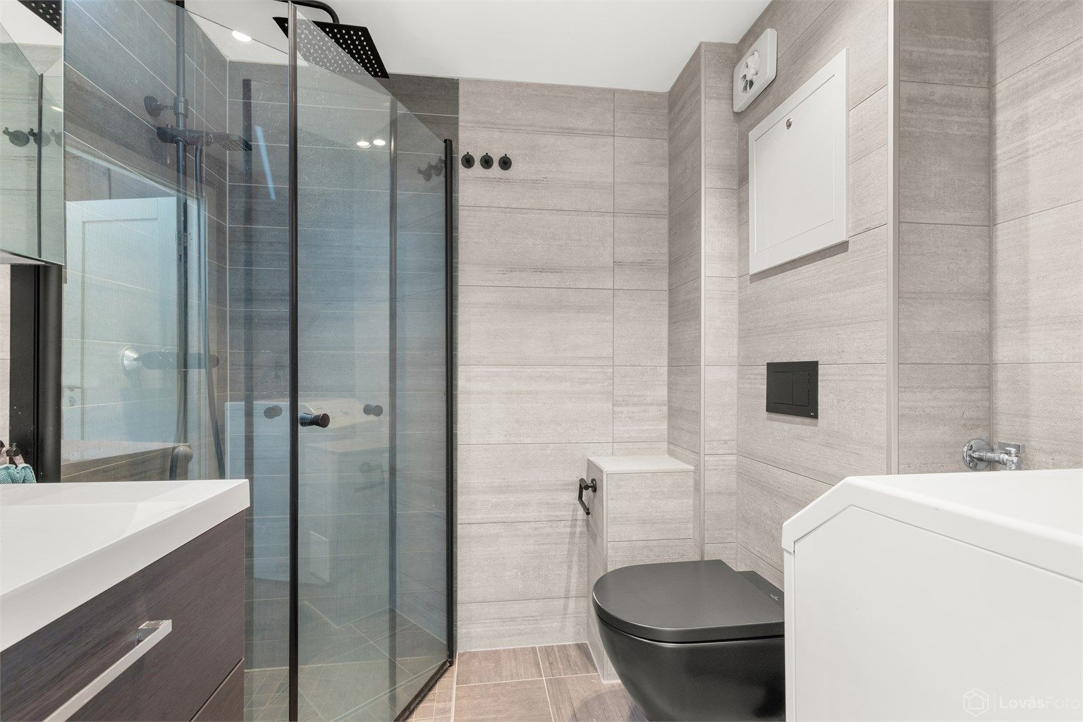 Rommet har dusjhjørne med glassdører, vegghengt toalett og opplegg for vaskemaskin.