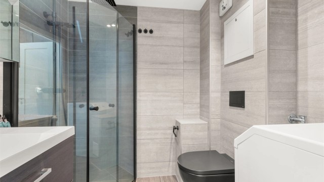 Rommet har dusjhjørne med glassdører, vegghengt toalett og opplegg for vaskemaskin.